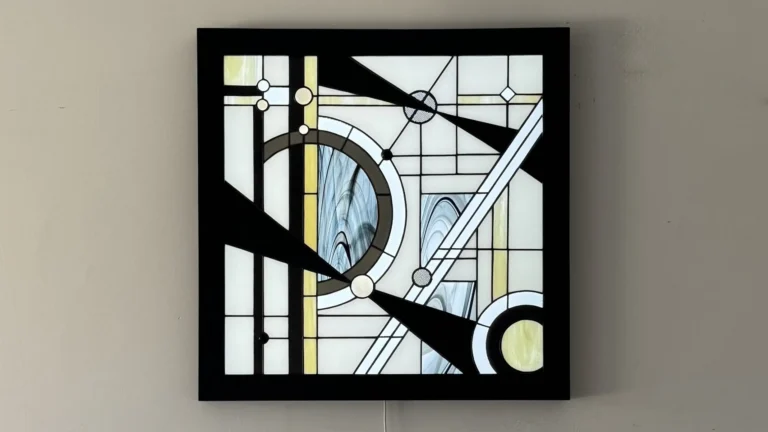 Tableau lumineux en vitrail Tiffany de style Art Déco, aux formes géométriques et verres opalescents, encadré de bois sombre et éclairé par une dalle LED.