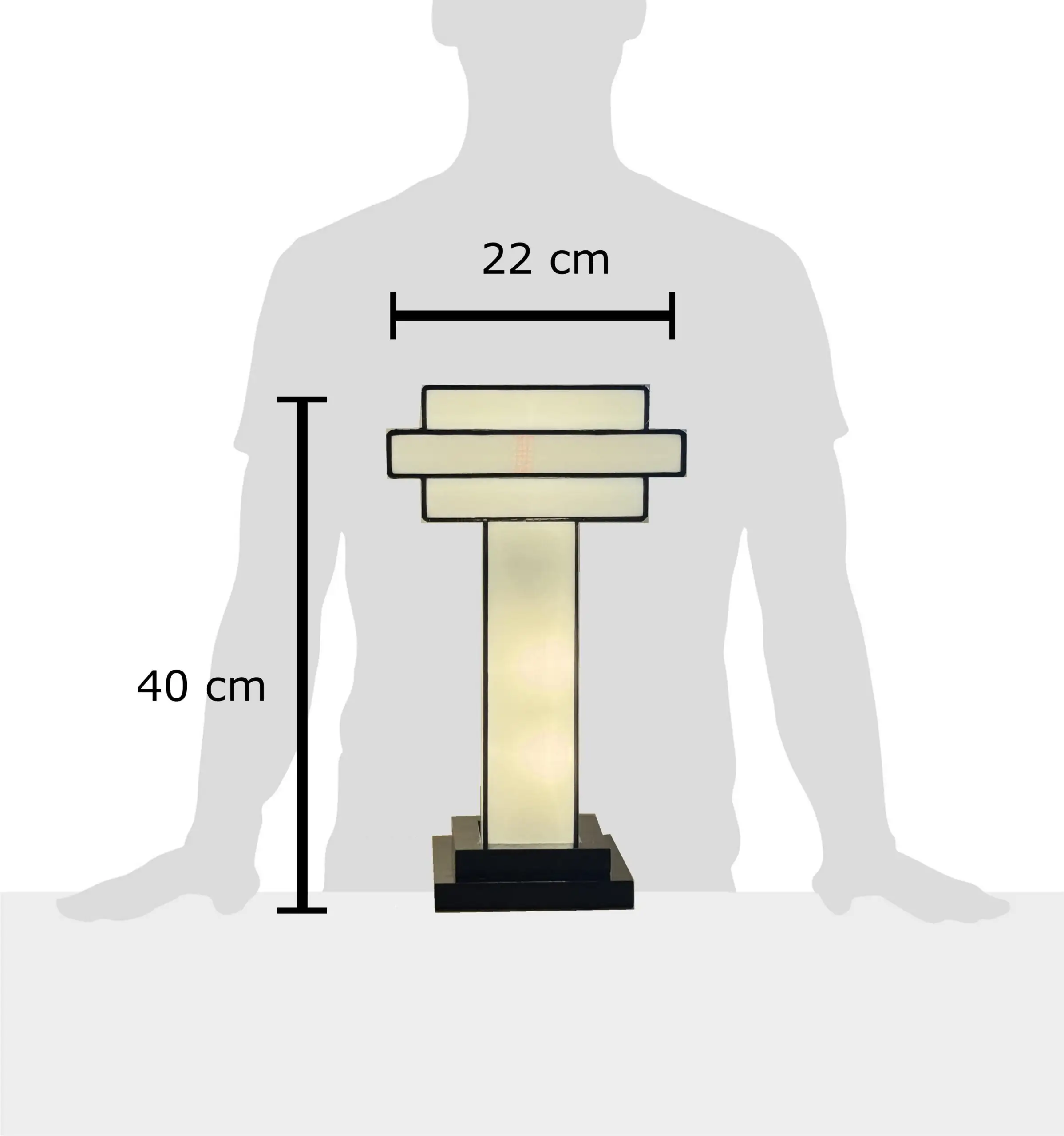 Lampe de table Art Déco en vitrail Tiffany, de forme cubique et étagée, évoquant un gratte-ciel stylisé. La base est carrée et noire. Un pilier vertical central en verre blanc dépoli s'élève vers un abat-jour composé de plusieurs plateaux carrés superposés, alternant entre le blanc opalescent et le noir opaque. Les soudures sont noires. La lampe est illuminée de l'intérieur, diffusant une lumière douce et homogène qui met en valeur sa géométrie architecturale et son contraste noir et blanc.