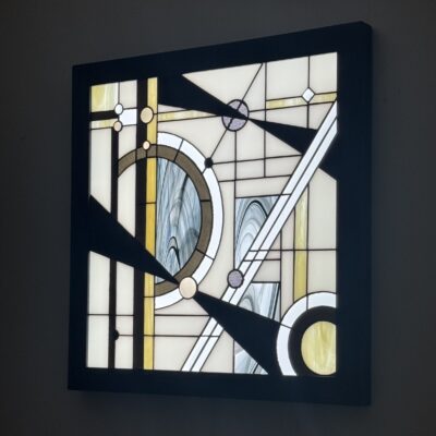 Tableau lumineux en vitrail Tiffany de style Art Déco, aux formes géométriques et verres opalescents, encadré de bois sombre et éclairé par une dalle LED.