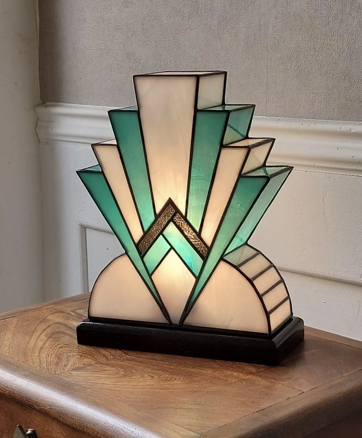 Lampe artisanale en vitrail Tiffany réversible en verre opalescent blanc et bleu canard avec touche de verre or, posée sur un socle en chêne massif sculpté teinté noir, diffusant une lumière chaleureuse.