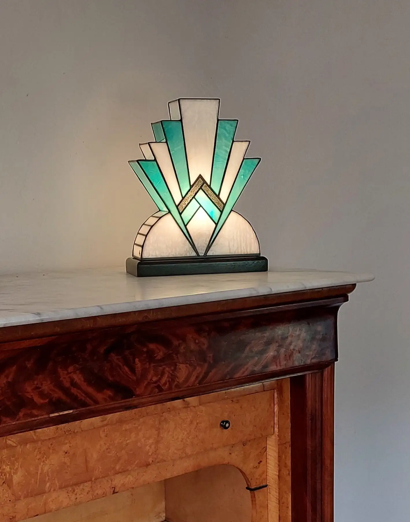 Lampe artisanale en vitrail Tiffany réversible en verre opalescent blanc et bleu canard avec touche de verre or, posée sur un socle en chêne massif sculpté teinté noir, diffusant une lumière chaleureuse.