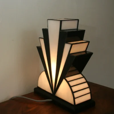 Lampe artisanale réversible en verres opalescents blanc pur et noir laqué, avec une subtile touche de verre gris diffusant une lumière chaleureuse, présentée sur un socle en chêne massif sculpté teinté noir, au design graphique et élégant.