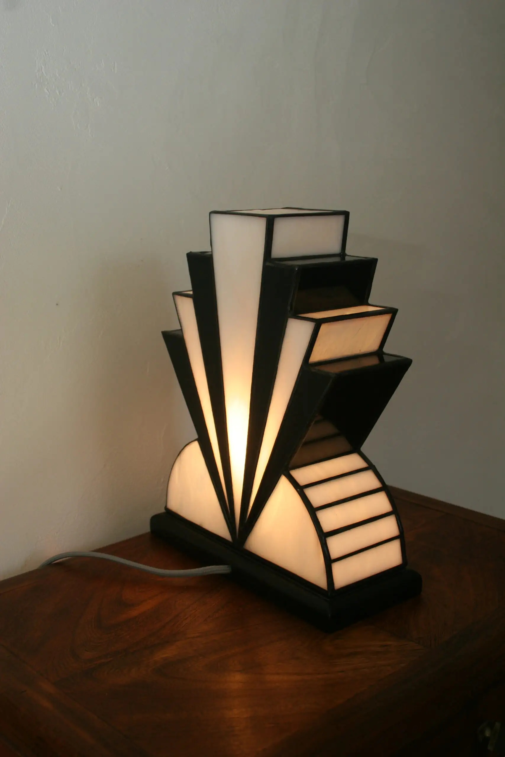 Lampe artisanale réversible en verres opalescents blanc pur et noir laqué, avec une subtile touche de verre gris diffusant une lumière chaleureuse, présentée sur un socle en chêne massif sculpté teinté noir, au design graphique et élégant.