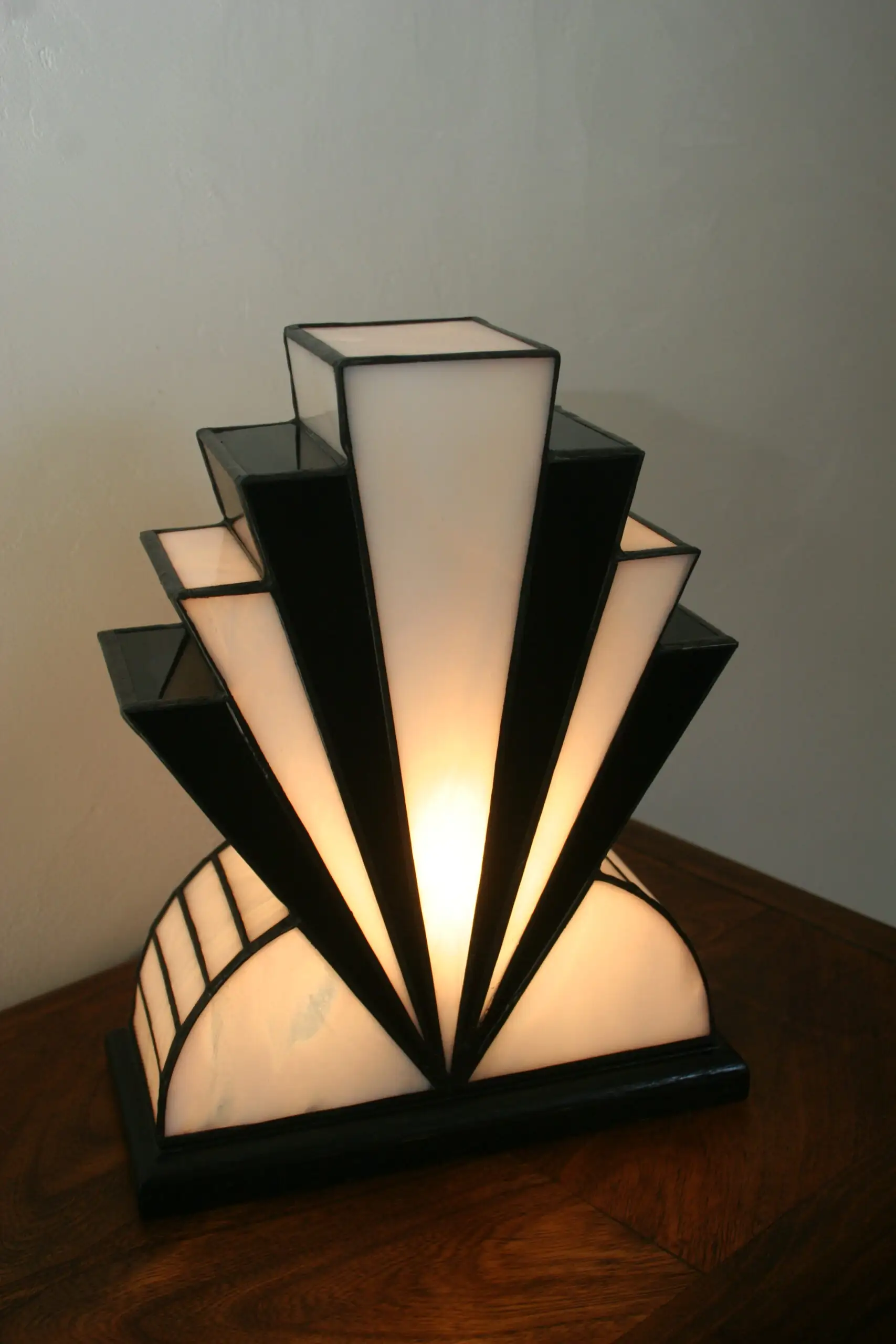 Lampe artisanale réversible en verres opalescents blanc pur et noir laqué, avec une subtile touche de verre gris diffusant une lumière chaleureuse, présentée sur un socle en chêne massif sculpté teinté noir, au design graphique et élégant.