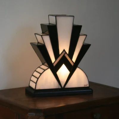 Lampe artisanale réversible en verres opalescents blanc pur et noir laqué, avec une subtile touche de verre gris diffusant une lumière chaleureuse, présentée sur un socle en chêne massif sculpté teinté noir, au design graphique et élégant.