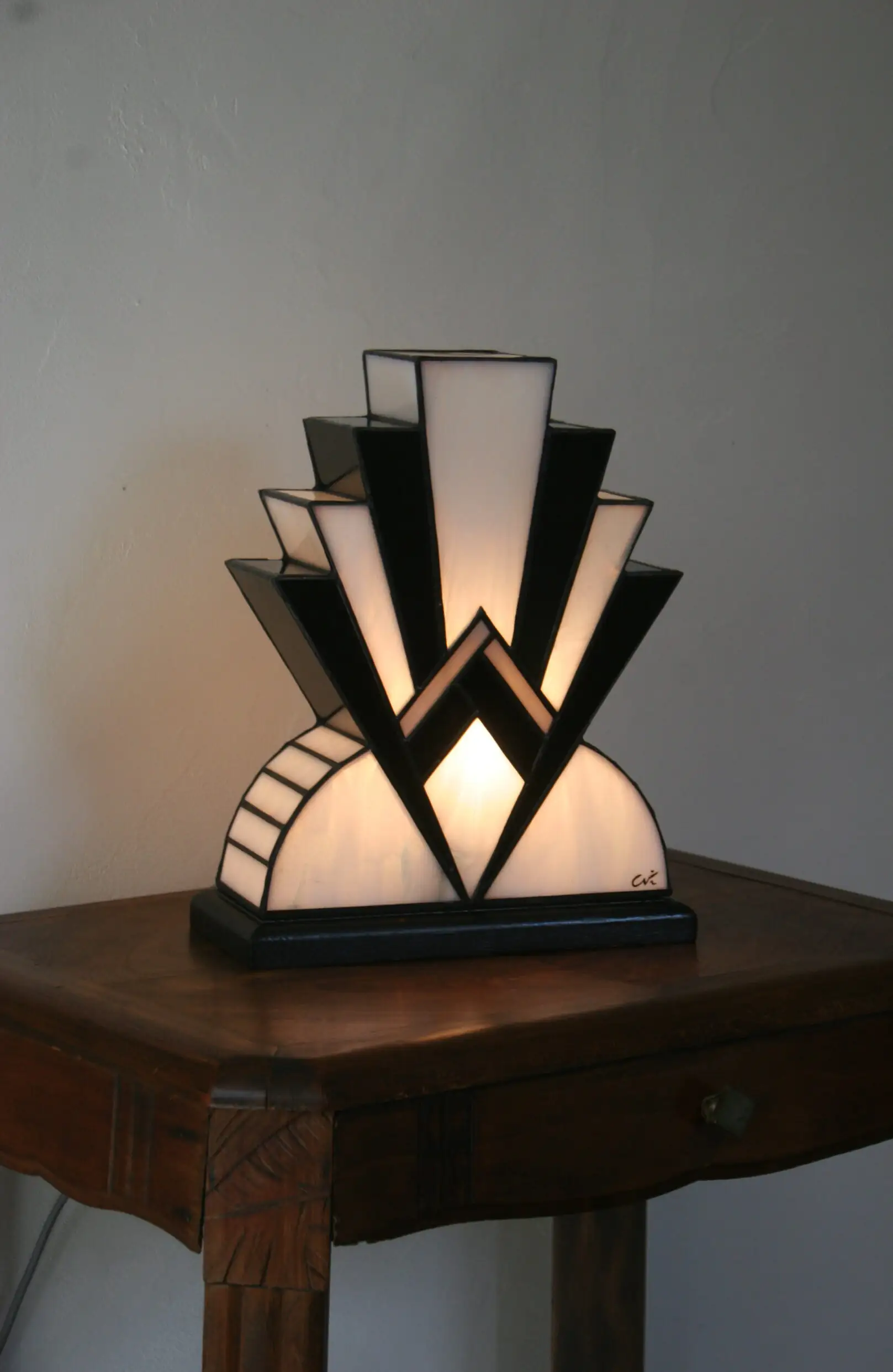 Lampe artisanale réversible en verres opalescents blanc pur et noir laqué, avec une subtile touche de verre gris diffusant une lumière chaleureuse, présentée sur un socle en chêne massif sculpté teinté noir, au design graphique et élégant.