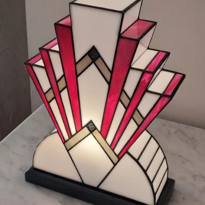 Lampe Art déco en vitrail aux formes géométriques, composée de verres opalescents blancs et rose vif avec inserts dorés, posée sur un socle en chêne massif patiné gris fer.