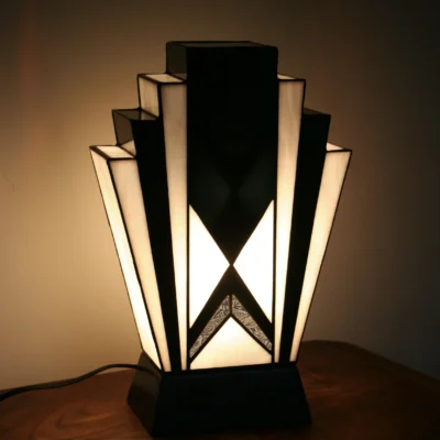 Lampe Tiffany Art Déco en vitrail opalescent blanc et noir avec socle en chêne massif sculpté diffusant une lumière chaleureuse.