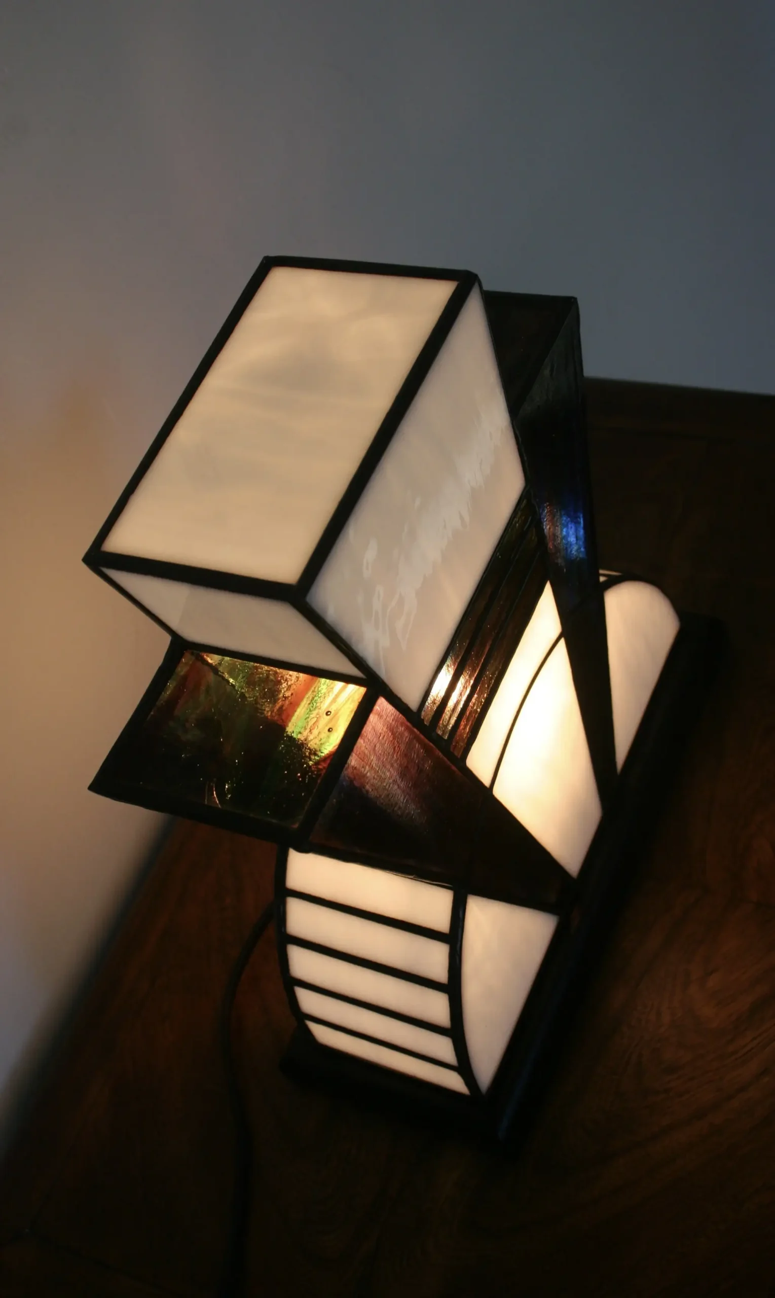 Lampe artisanale en verre opalescent blanc et pourpre, striée de vert et de bleu, à l’aspect poudré et légèrement vieilli, diffusant une lumière douce et chaleureuse.