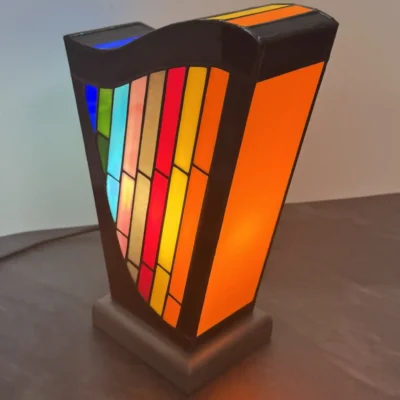 Lampe d’art contemporain Harpège Zénith en vitrail Tiffany, forme de harpe, verres opalescents multicolores sur structure noire et socle en béton ciré.