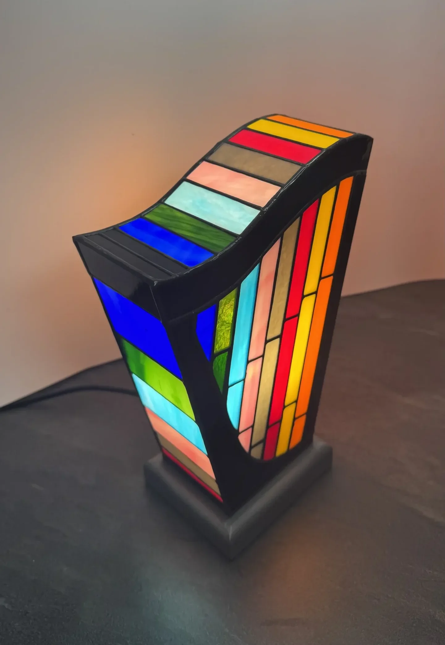 Lampe d’art contemporain Harpège Zénith en vitrail Tiffany, forme de harpe, verres opalescents multicolores sur structure noire et socle en béton ciré.