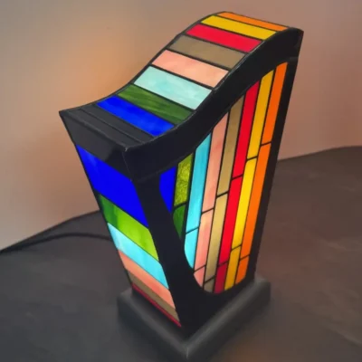Lampe d’art contemporain Harpège Zénith en vitrail Tiffany, forme de harpe, verres opalescents multicolores sur structure noire et socle en béton ciré.