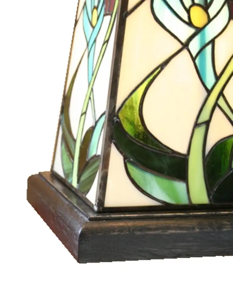 Grande lampe de table ou de bureau en vitrail Tiffany de style Art Nouveau. Elle possède un pied et un abat-jour de forme pyramidale et carrée. L'abat-jour et la base sont décorés de motifs floraux (probablement des arums ou des lys calla) aux teintes pastel de rose, bleu/turquoise, et jaune pâle, sur un fond de verre blanc opalescent. Des bandes de verre vert foncé encadrent la base et les bords de l'abat-jour. La lampe est posée sur une petite table d'appoint en bois avec un pied sculpté, et elle diffuse une lumière chaude