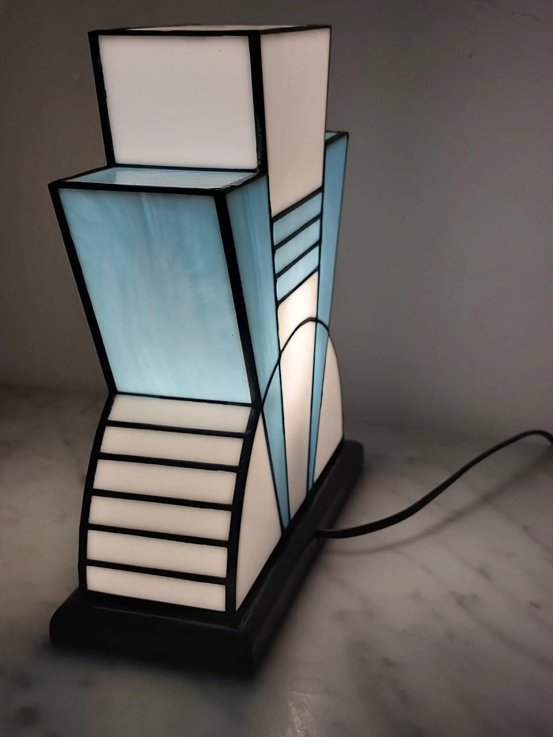 Lampe Art Déco vitrail Tiffany 1926 bleu baltique et blanc, verre opalescent géométrique, socle en chêne massif sculpté noir, fabrication artisanale française.