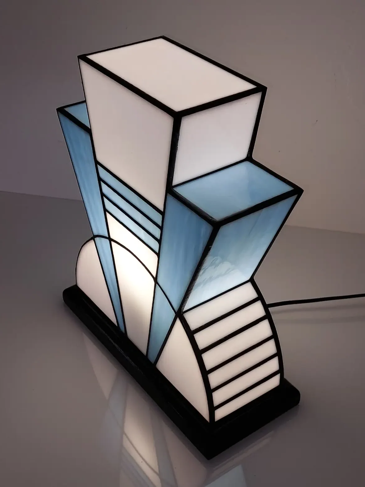 Lampe Art Déco vitrail Tiffany 1926 bleu baltique et blanc, verre opalescent géométrique, socle en chêne massif sculpté noir, fabrication artisanale française.