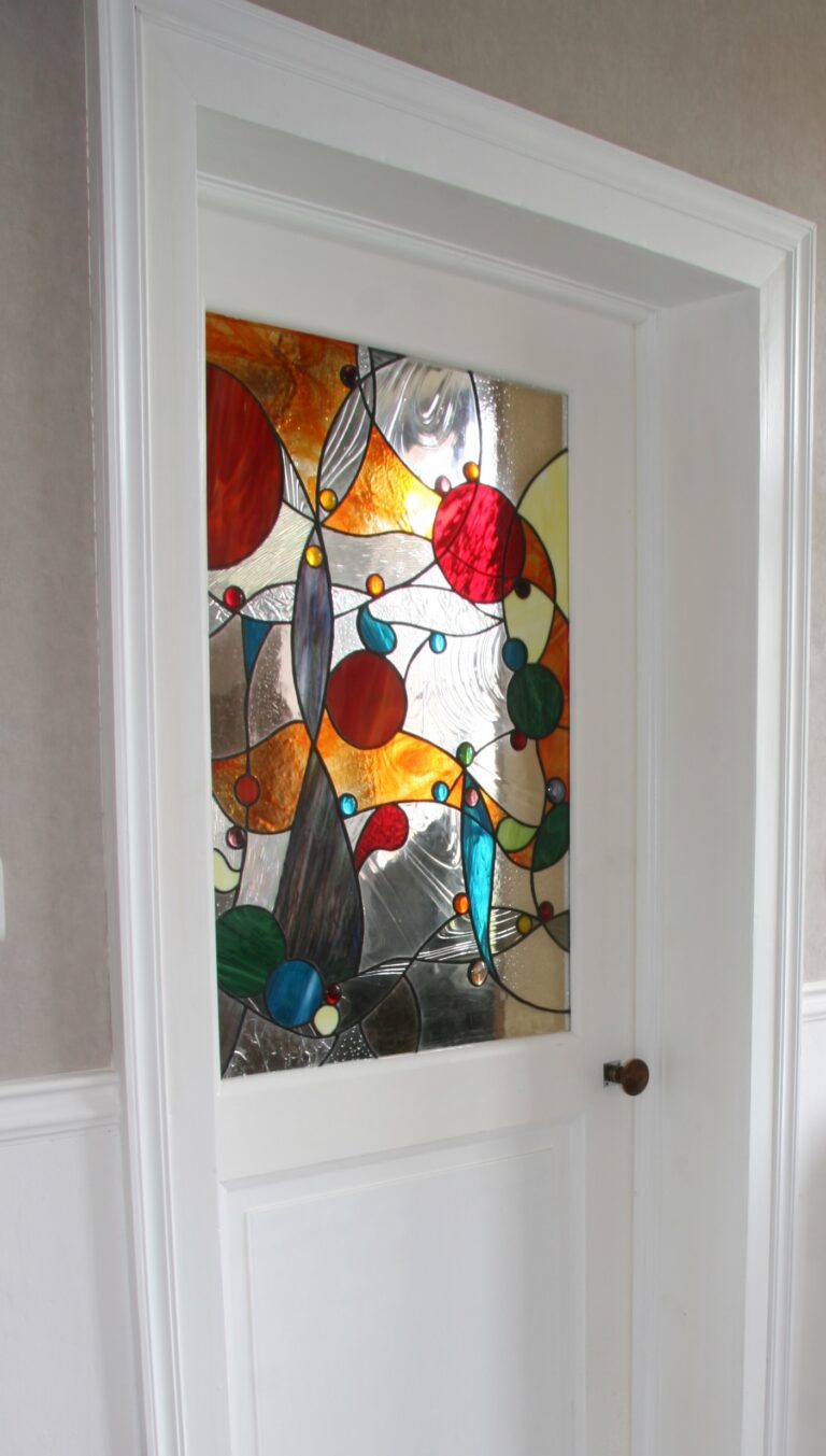 Porte intérieure blanche avec panneau en vitrail coloré abstrait, apportant lumière et élégance à une entrée lumineuse au sol damier.
