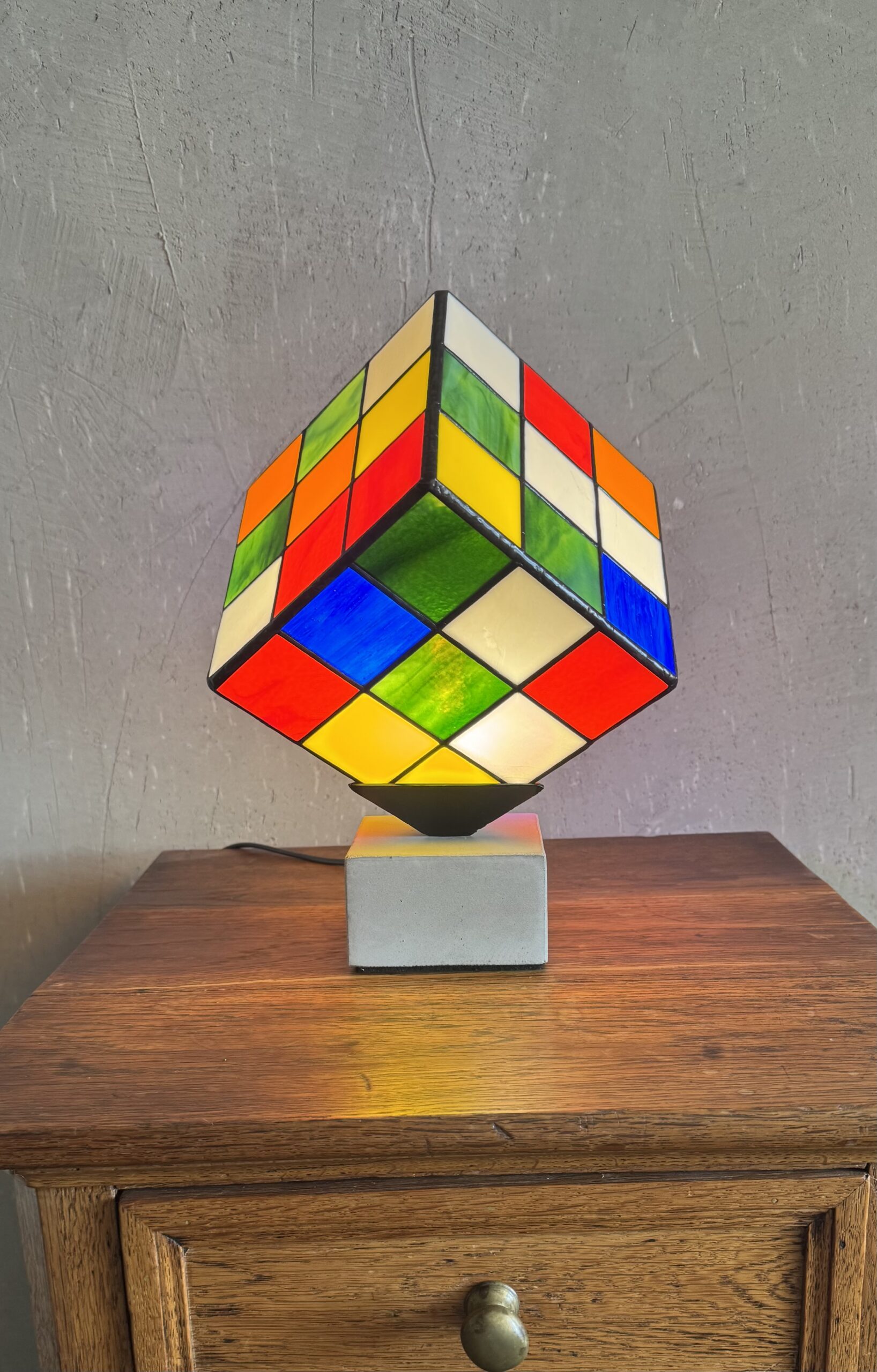 Lampe Rubik's Cube en vitrail Tiffany sur socle béton, luminaire artisanal français multicolore de style design contemporain.