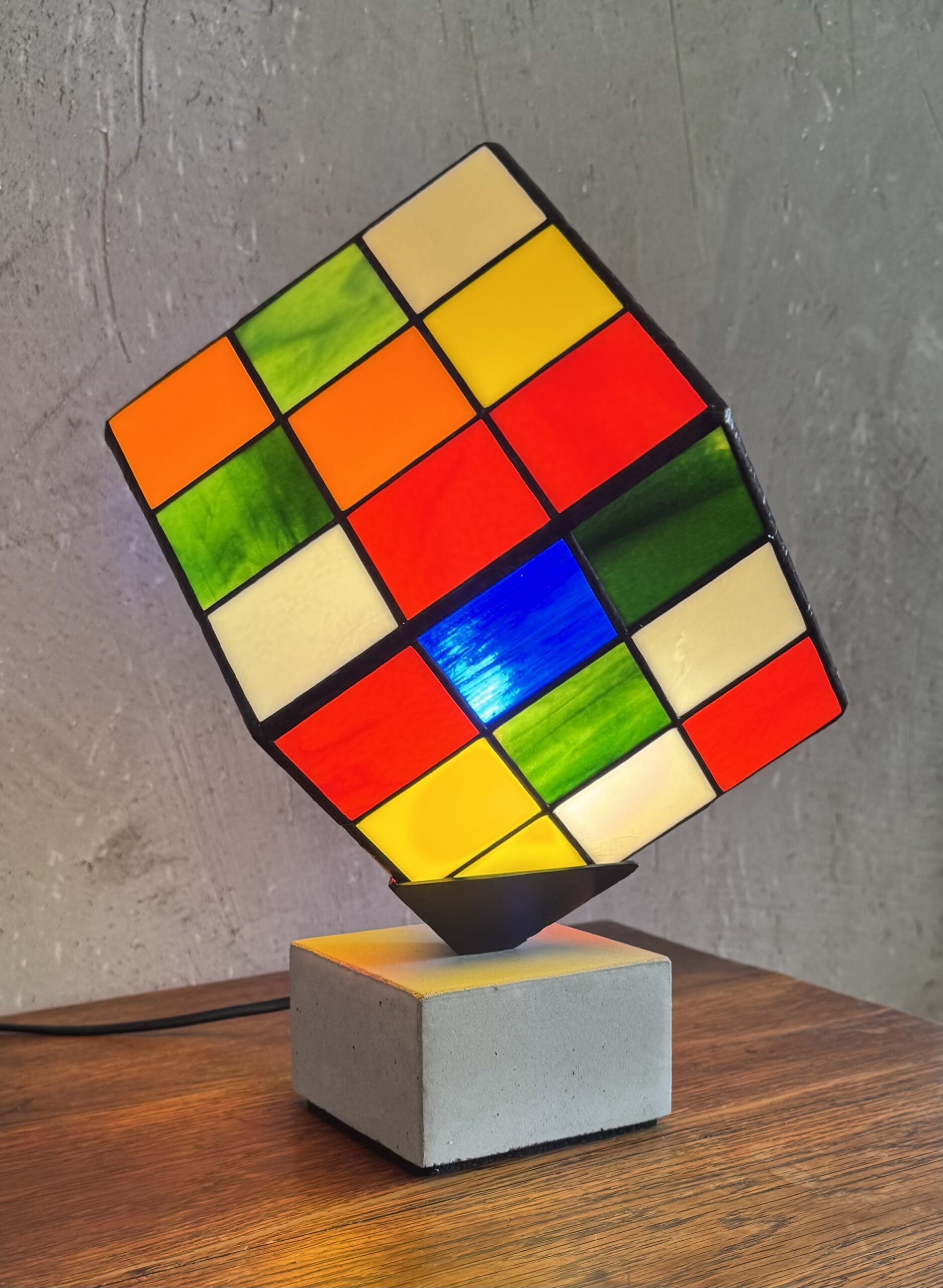 Lampe Rubik's Cube en vitrail Tiffany sur socle béton, luminaire artisanal français multicolore de style design contemporain.