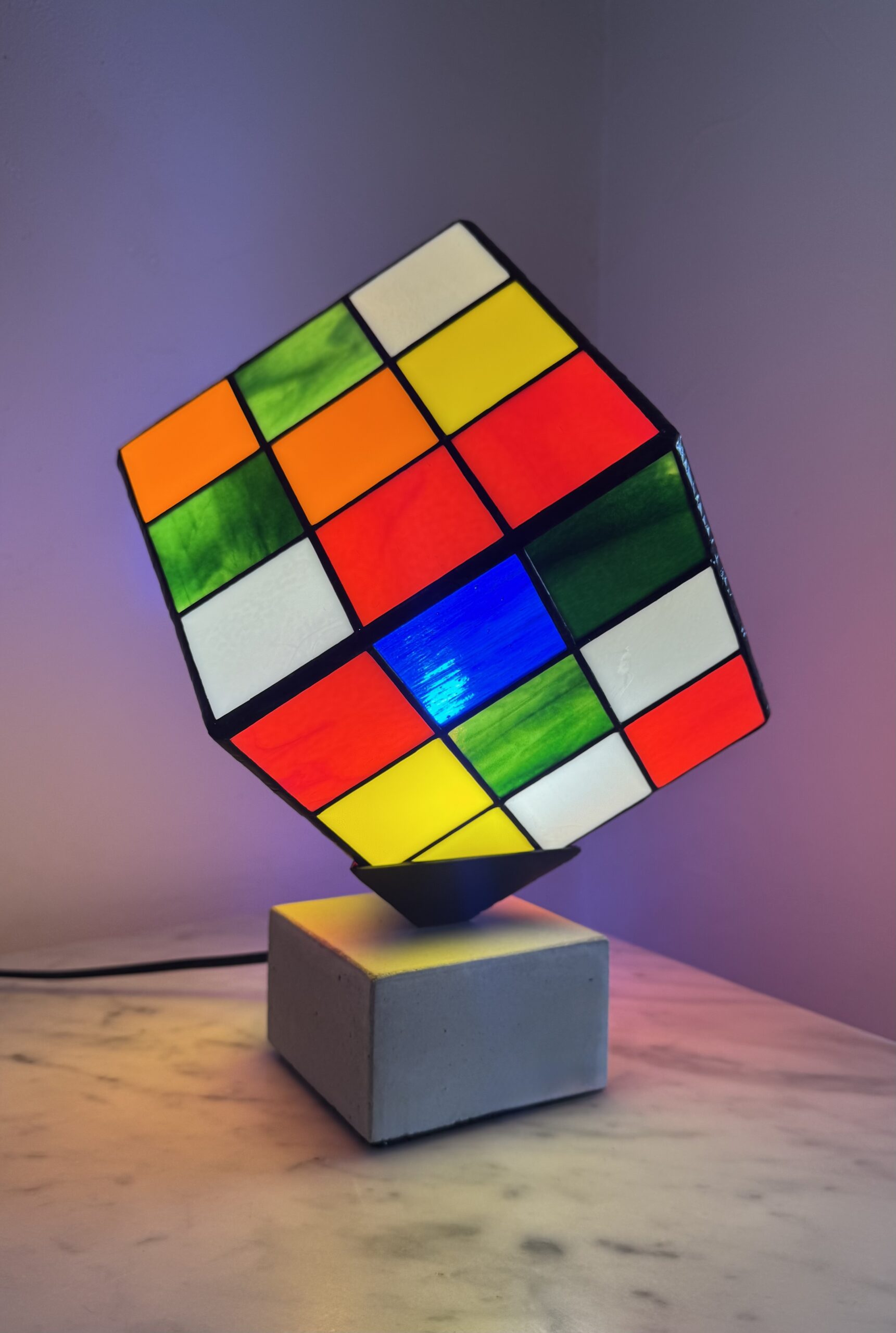 Lampe Rubik's Cube en vitrail Tiffany sur socle béton, luminaire artisanal français multicolore de style design contemporain.