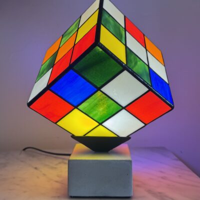 Lampe Rubik's Cube en vitrail Tiffany sur socle béton, luminaire artisanal français multicolore de style design contemporain.