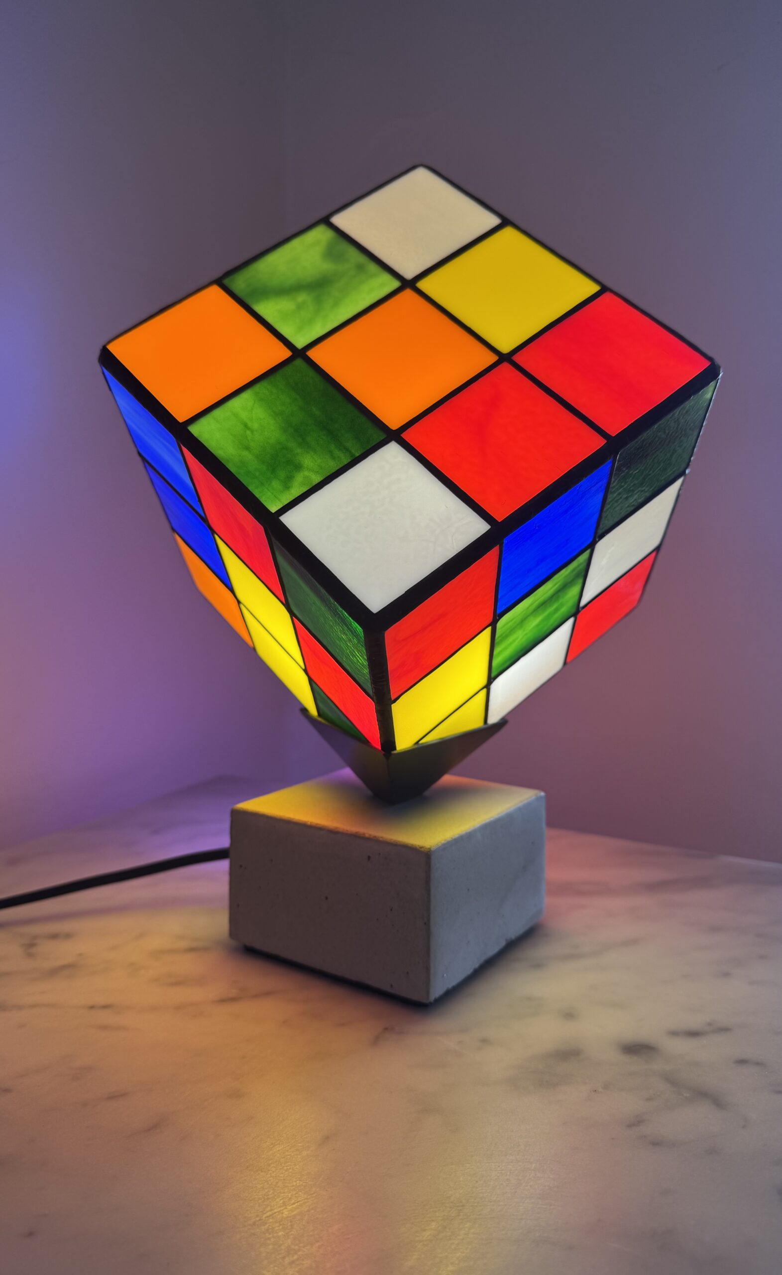 Lampe Rubik's Cube en vitrail Tiffany sur socle béton, luminaire artisanal français multicolore de style design contemporain.