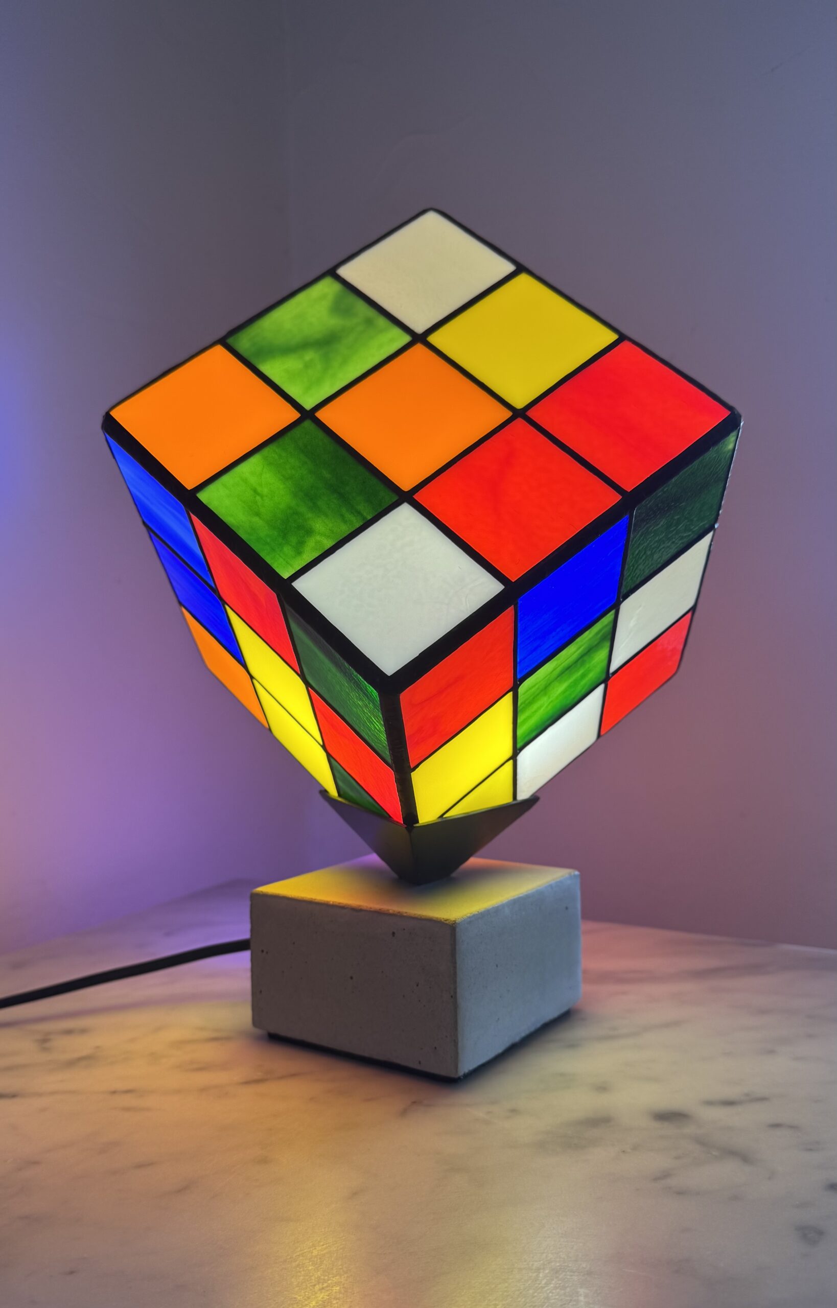 Lampe Rubik's Cube en vitrail Tiffany sur socle béton, luminaire artisanal français multicolore de style design contemporain.