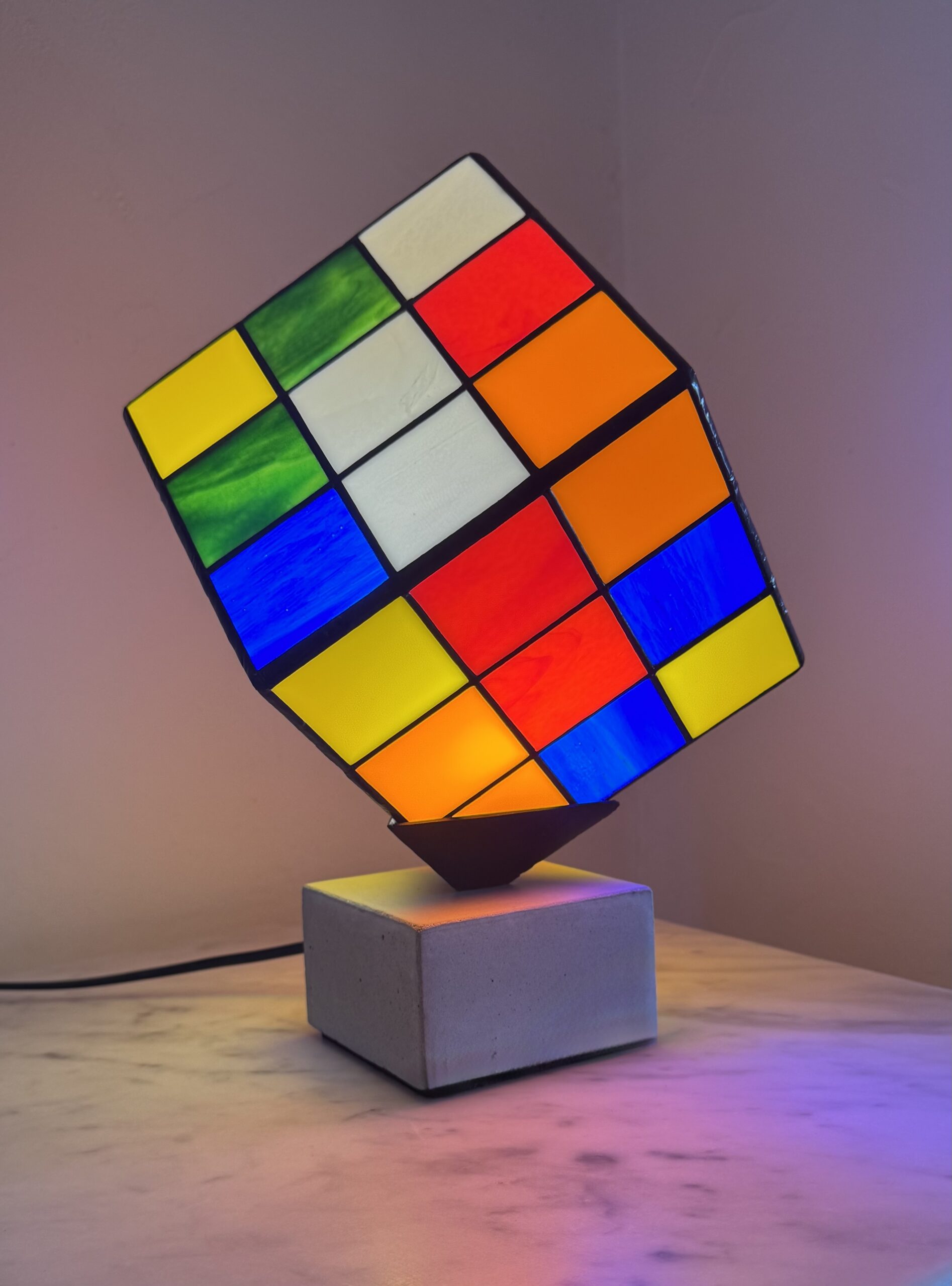 Lampe Rubik's Cube en vitrail Tiffany sur socle béton, luminaire artisanal français multicolore de style design contemporain.